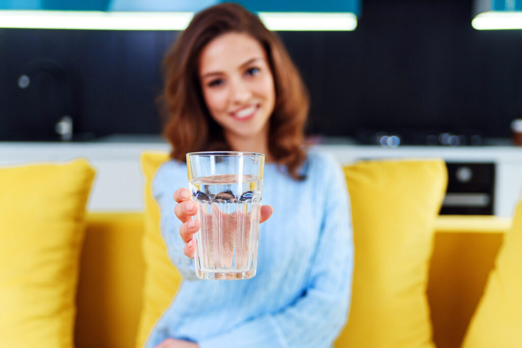 Frau hält gefülltes Wasserglas in die Kamera.