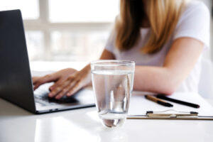 Frau arbeitet am Computer und ein Wasserglas steht neben ihr.