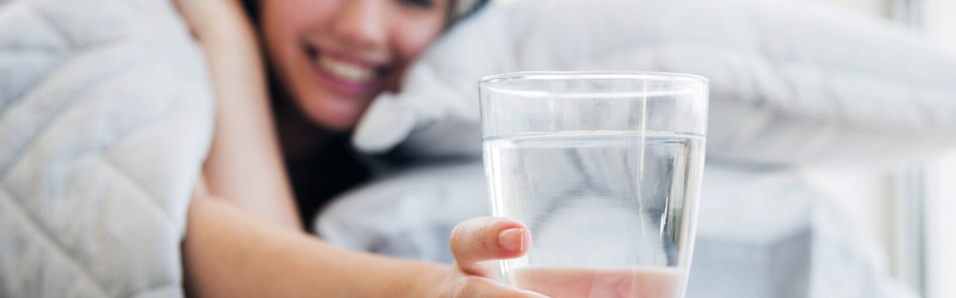 Frau im Bett greift nach Wasserglas auf Nachttisch.