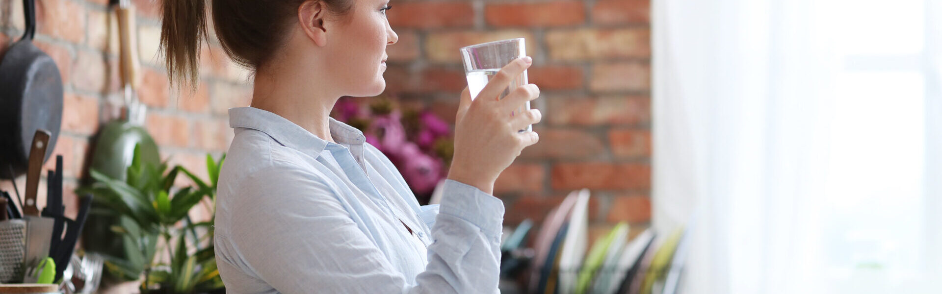 Frau in der Küche mit Wasserglas.