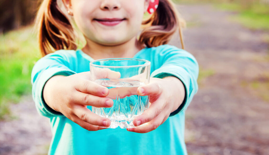 Kind hält ein Wasserglas in die Kamera.