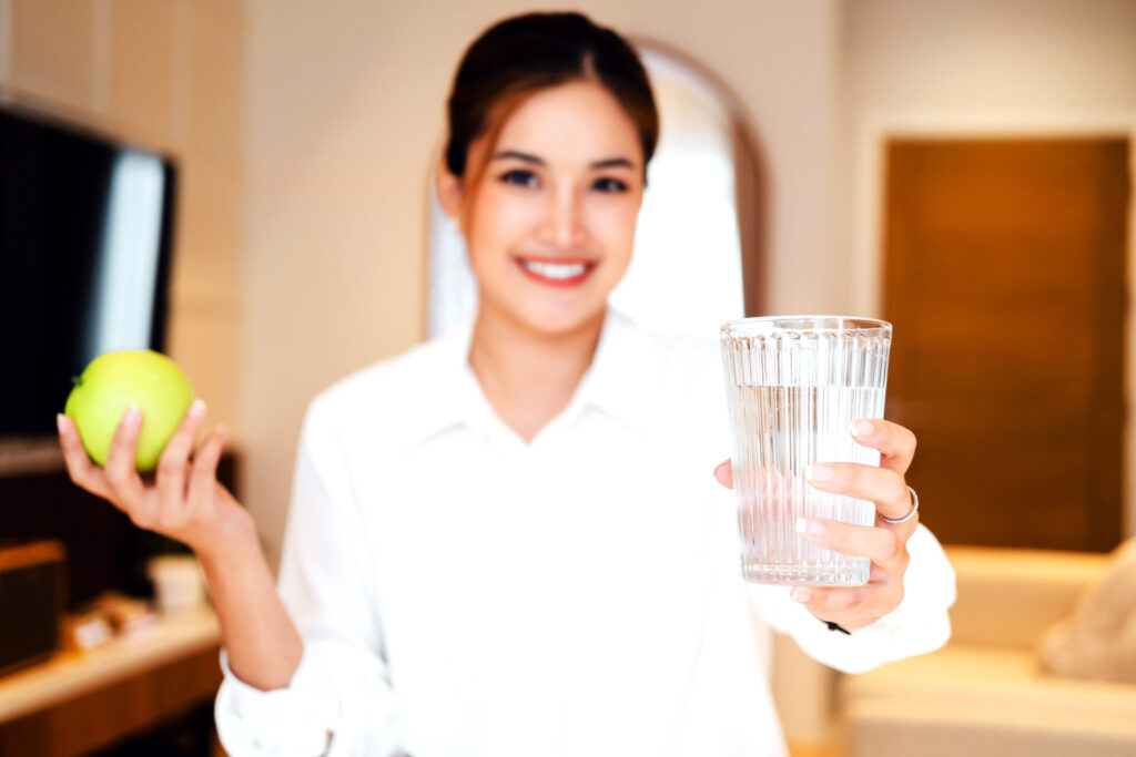 Frau hält Apfel und Wasserglas in den Händen.