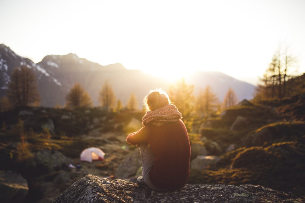 Stimmungsbild: Ruhiges Bergpanaorama, davor sitzt Frau mit Rücken zur Kamera und genießt Ausblick.