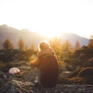 Stimmungsbild: Ruhiges Bergpanaorama, davor sitzt Frau mit Rücken zur Kamera und genießt Ausblick.