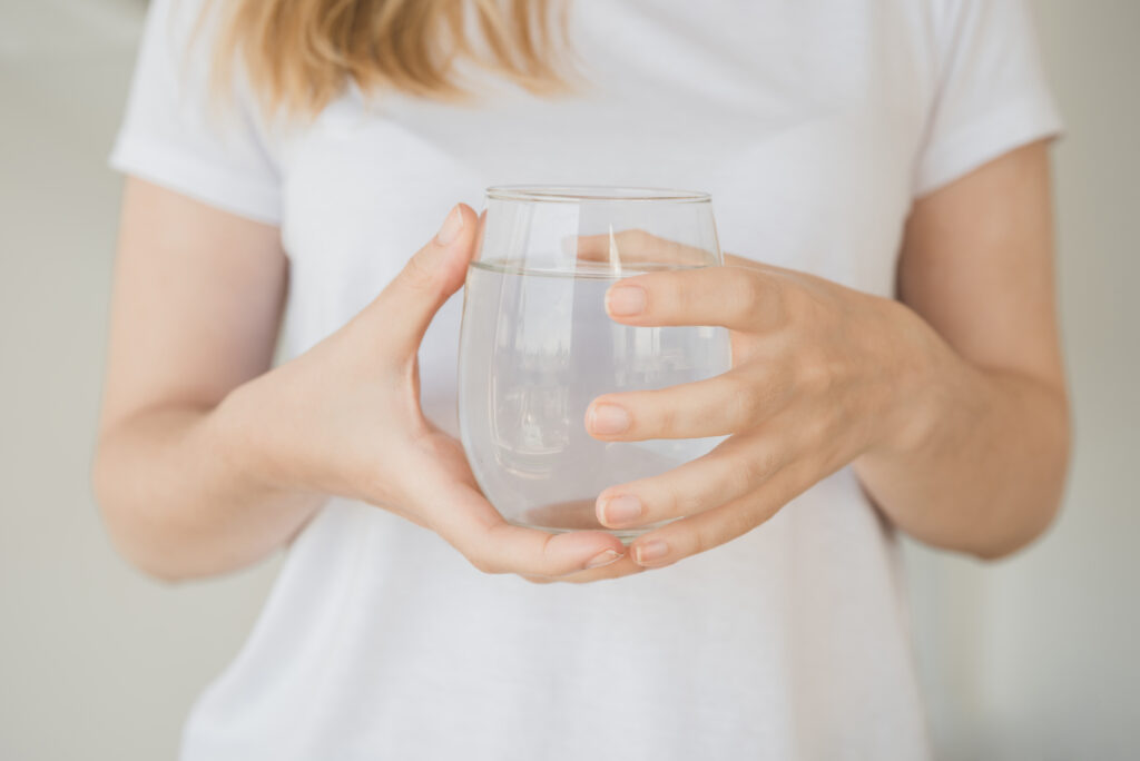 Stimmungsbild: Junge Frau hält Wasserglas mit beiden Händen.