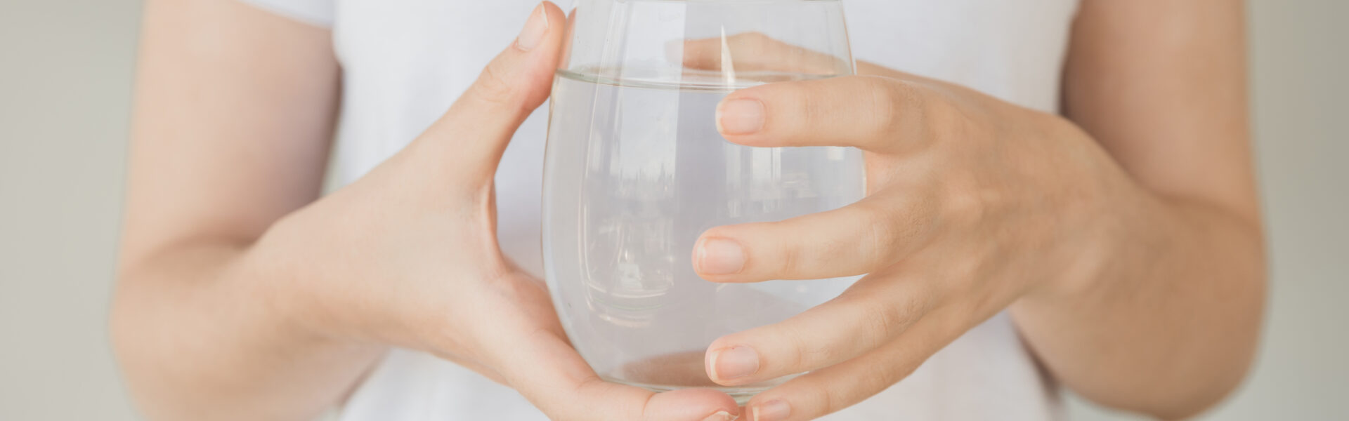 Stimmungsbild: Junge Frau hält Wasserglas mit beiden Händen.