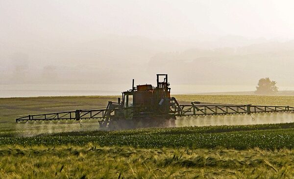 Traktor fährt über ein Feld und versprüht Pestizide.