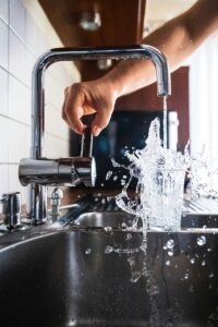 Wasser sprudelt aus einem Wasserhahn in ein Wasserglas und läuft über.